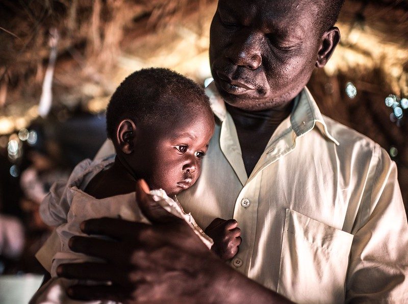 Joseph Malis, 39, holds his daughter in Bidi Bidi refugee camp, Uganda. Photo : Tommy Trenchard